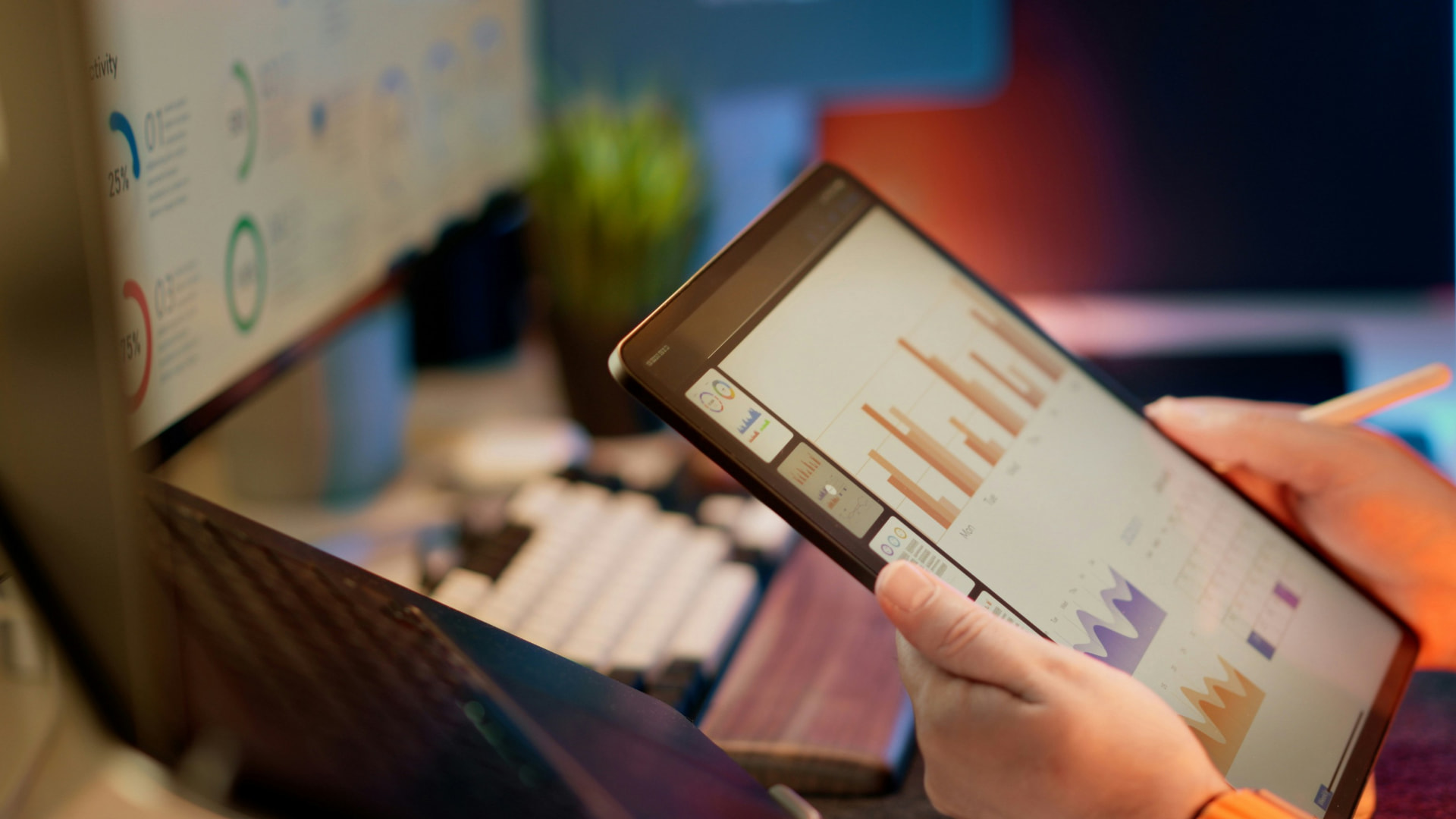 Hands reviewing operational charts on a tablet beside a desktop dashboard